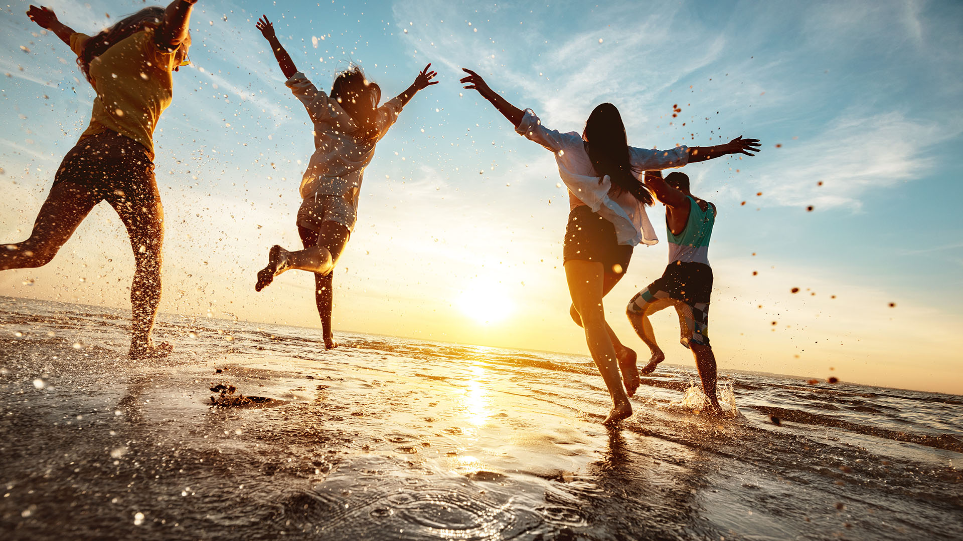 Four happy friends at sunset beach party runs to water