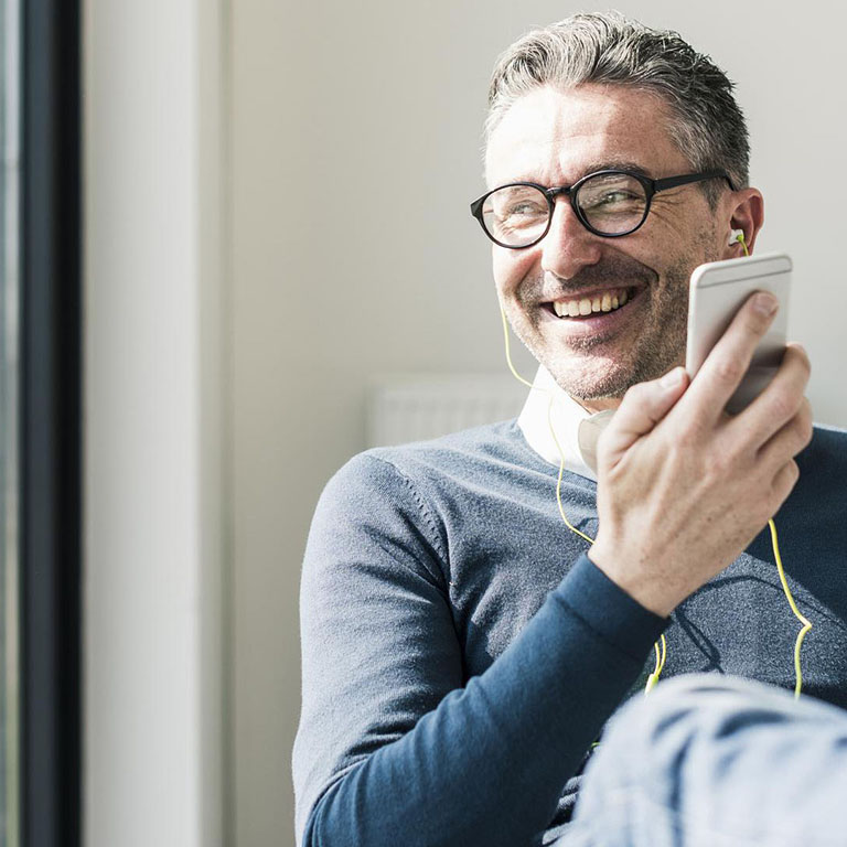 Man with glasses with a smartphone smiling on a sofa