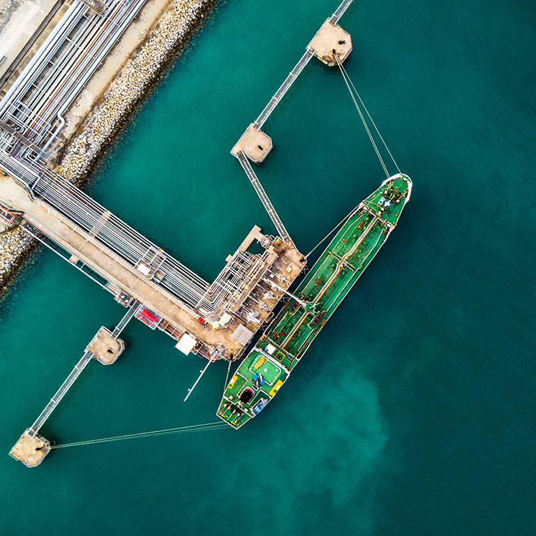 Aerial top view of green oil tanker cargo vessel under cargo operations on typical shore station.