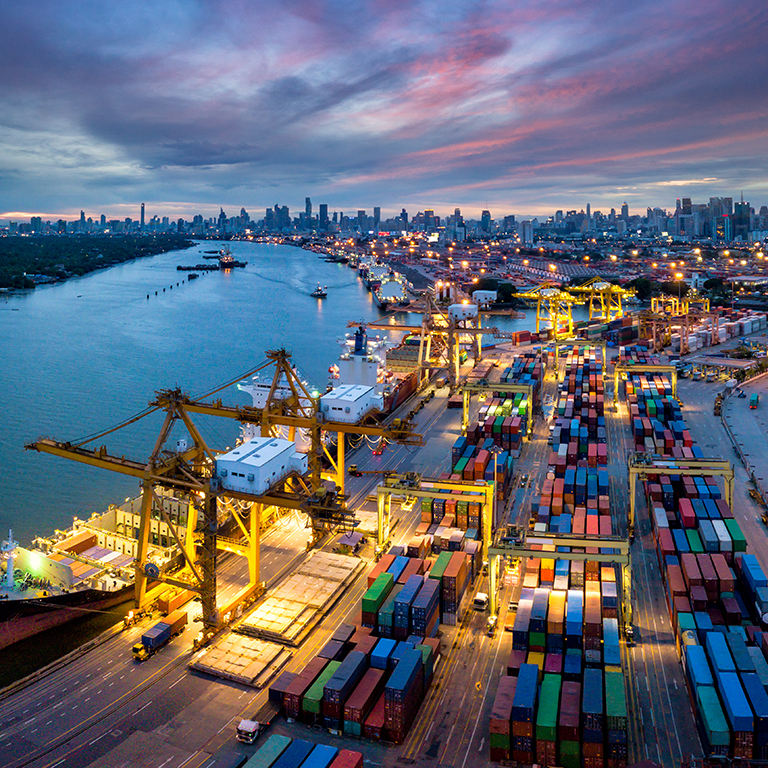 Aerial view of international port with Crane loading containers in import export business logistics with cityscape of Bangkok city Thailand at night