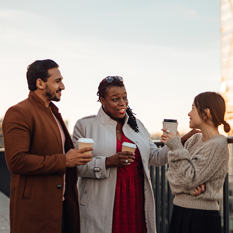 Cheerful multi-ethnic business people standing by railing at rooftop during coffee break.