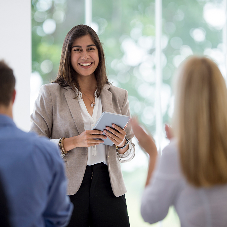 Business professionals clapping at a presentation from a colleague during a meeting in the boardroom.