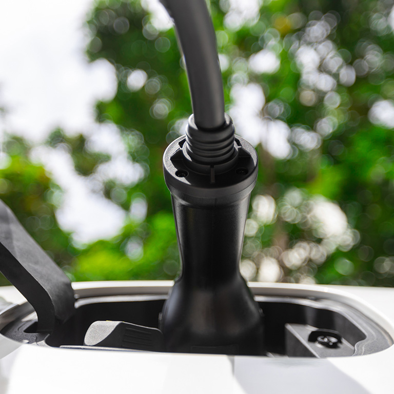 Closeup EV charger plugged into electric vehicle socket at charging station image from below view as progressive concept of eco-friendly car powered by sustainable and renewable energy.