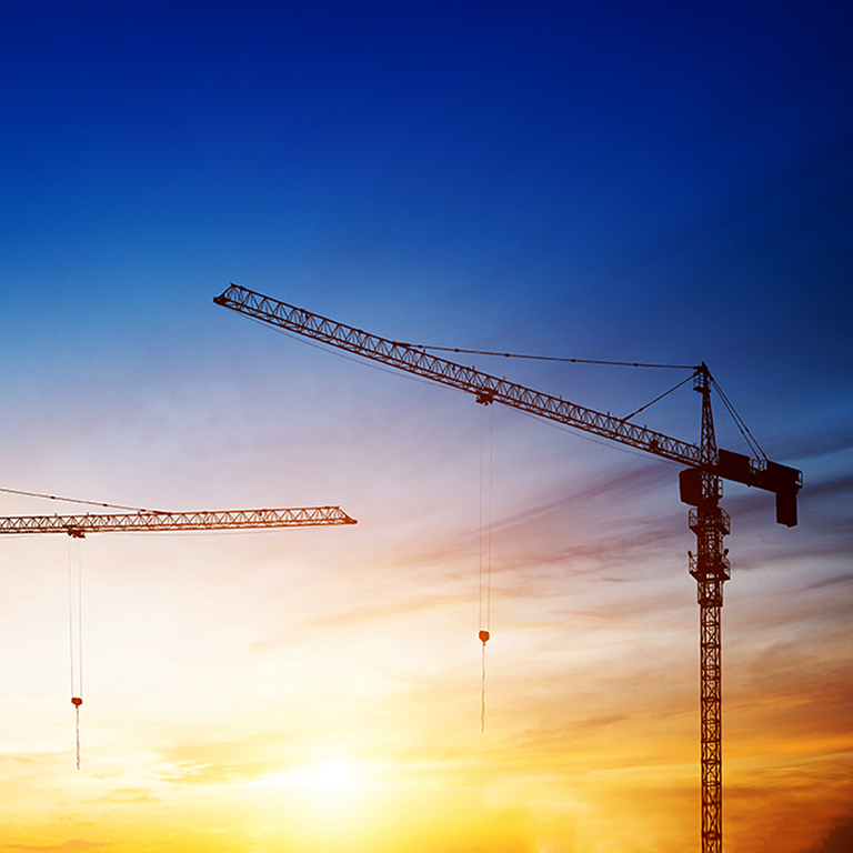 Industrial construction cranes and building silhouettes over sun at sunrise.