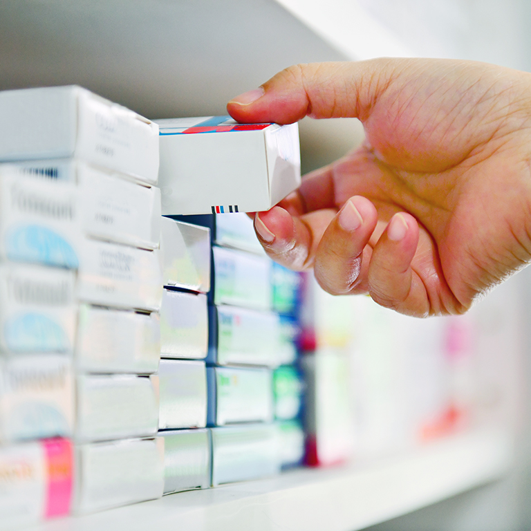 Closeup pharmacist hand holding medicine box in a pharmacy drugstore.