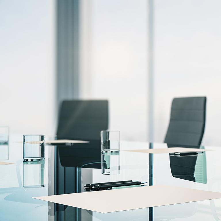 Light and airy boardroom with glass table with paper, pen and water glasses.