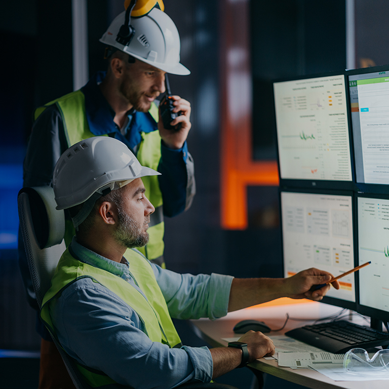 Main engineer and workers operator wearing safety vests and hard hats control product process on factory uses SCADA system and industry 4.0. Two operators follow assembly line using screens with UI