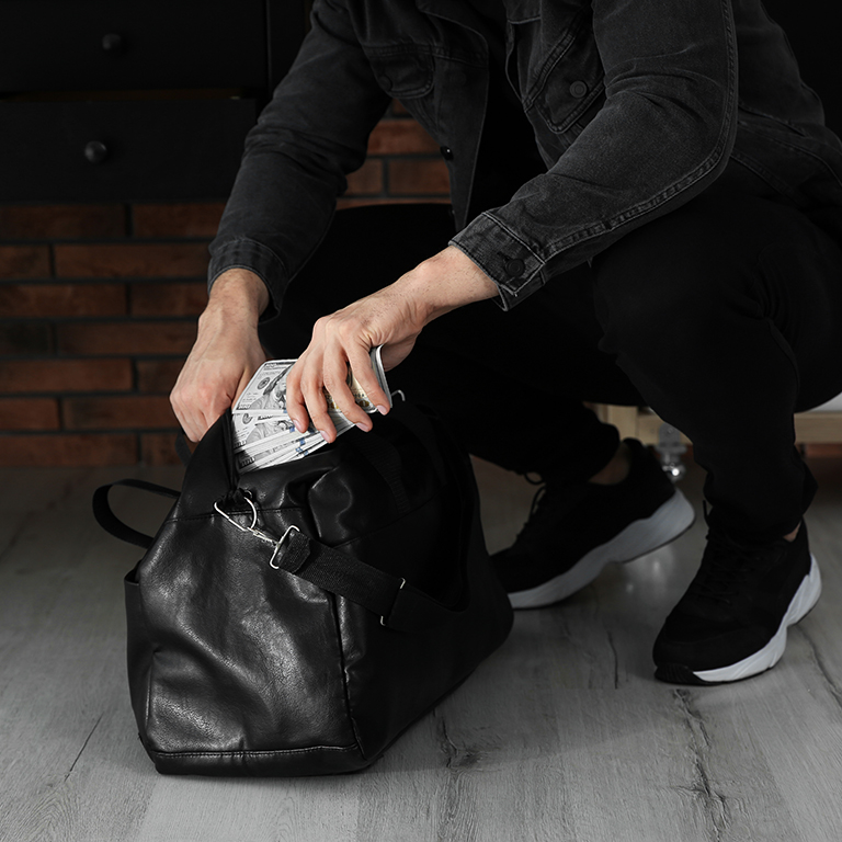 Close up of a man with dark clothing putting money in a bag indoors.