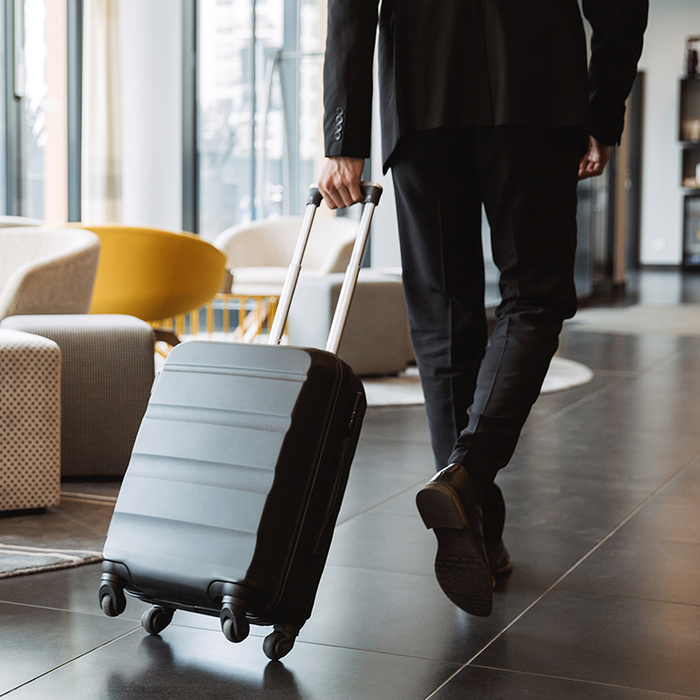 Cropped photo of a businessman wearing suit walking with suitcase in hotel lobby