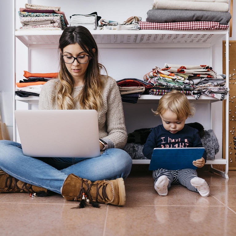 Mother and little daughter sitting on the floor at home using laptop and tablet
