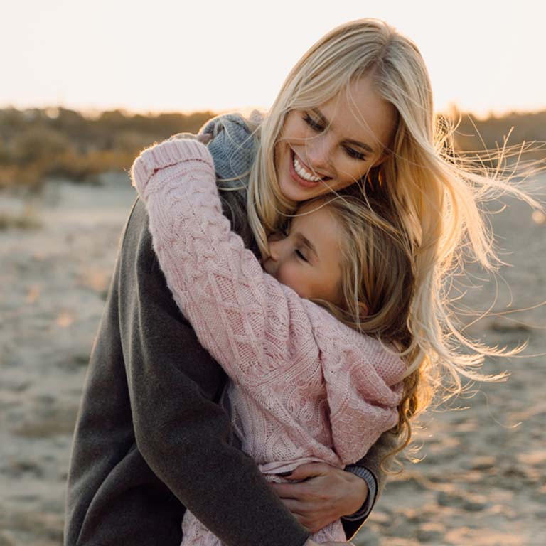 happy mother embracing her daughter on seashore
