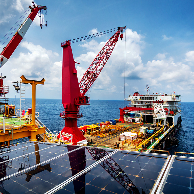 Offshore crane in oil platform with solar panels transfering material to a vessel