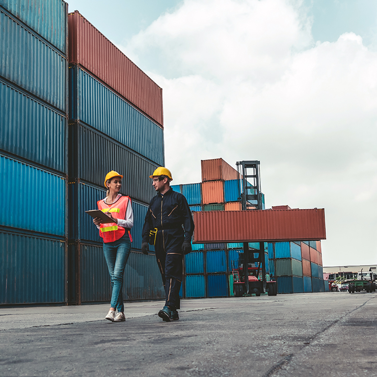 Industrial worker works with co-worker at overseas shipping container yard. Logistics supply chain management and international goods export concept .